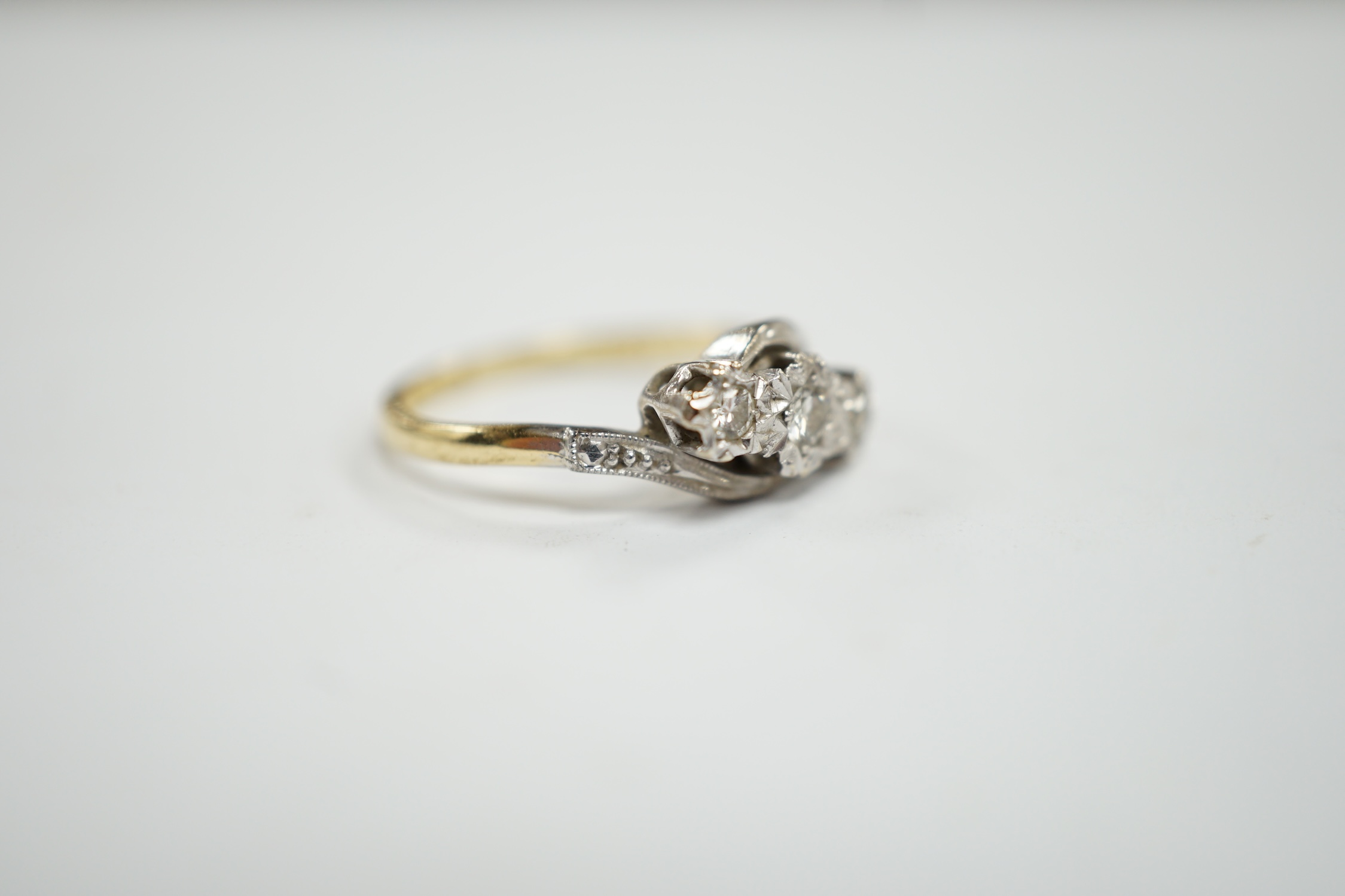 A mid to late 20th century 18ct gold and illusion set three stone diamond crossover ring, size N, gross weight 3.3 grams.